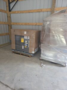 Two large items on pallets in a storage area, one wrapped in clear plastic and the other partially exposed with shipping labels attached.
