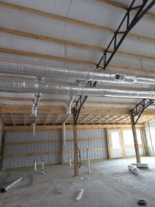 Interior of a building under construction showing exposed metal ductwork, unfinished walls, wooden beams, and a concrete floor.