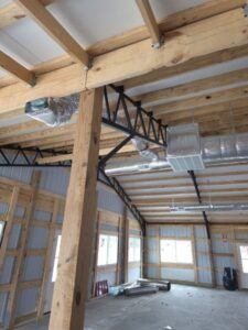 Interior of a partially constructed building with exposed wooden beams, metal supports, and visible ductwork along the ceiling.