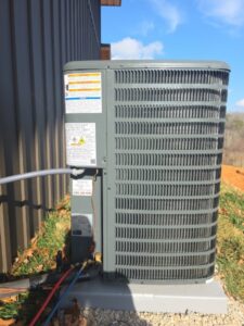 Outdoor air conditioning unit with connected refrigerant lines, situated on a concrete slab beside a building, under a clear sky.