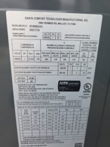 Label on a Daikin Comfort Technologies Manufacturing unit showing model info, specifications, electrical data, refrigerant type, and certification logos.