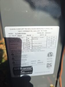Close-up of a Daikin Comfort Technologies Manufacturing, Inc. unit label showing model, serial number, electrical specs, compressor info, refrigerant type, and safety certifications.