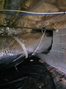 Exposed insulated HVAC duct runs through a crawl space with visible fiberglass insulation, concrete block wall, and plastic ground cover.