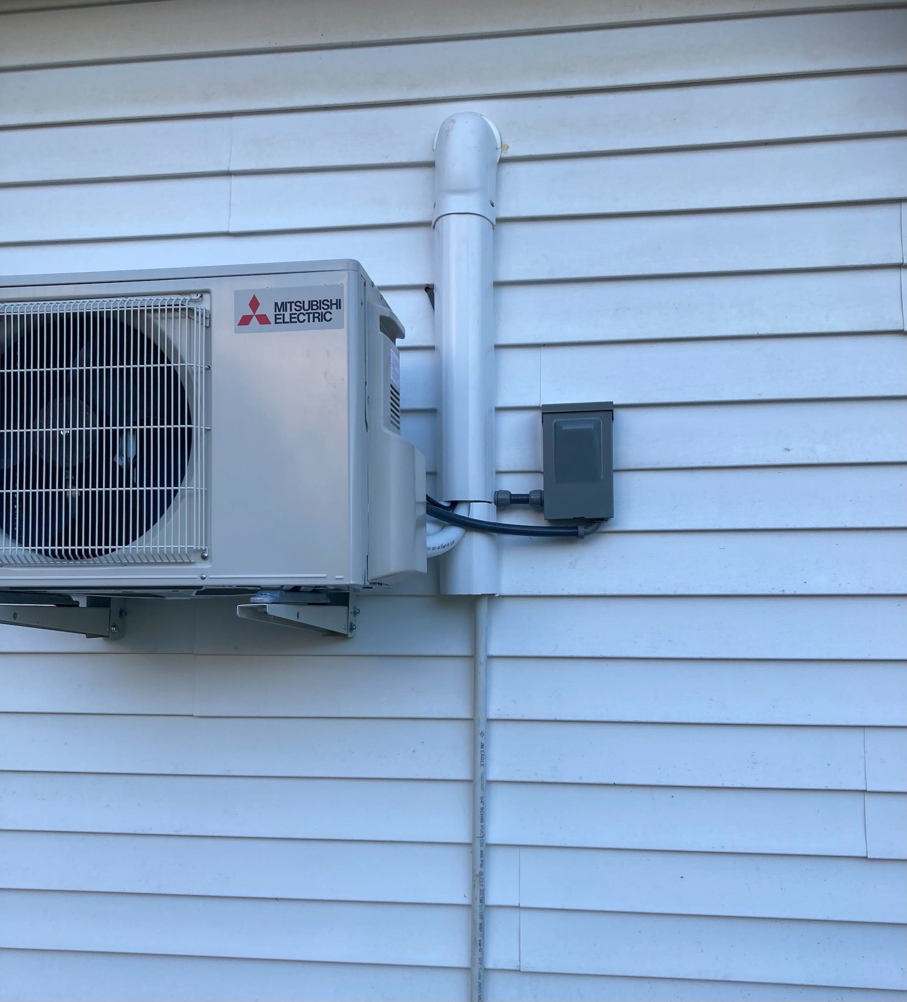 Outdoor Mitsubishi Electric unit featured in a mini-split installation, mounted on the exterior wall with conduit and electrical box attached to the home's white siding.