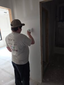 A person wearing a Buie's Heating & Air shirt adjusts a thermostat on a wall inside a building under construction or renovation.