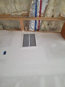 A wall vent is installed on a partially finished wall with visible insulation, ductwork, and exposed ceiling beams above.