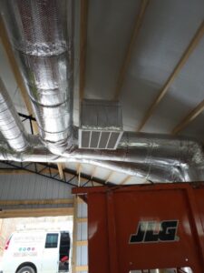 Large insulated air ducts run across a ceiling with a vent in the center; a JLG machine and part of a service van are visible below.