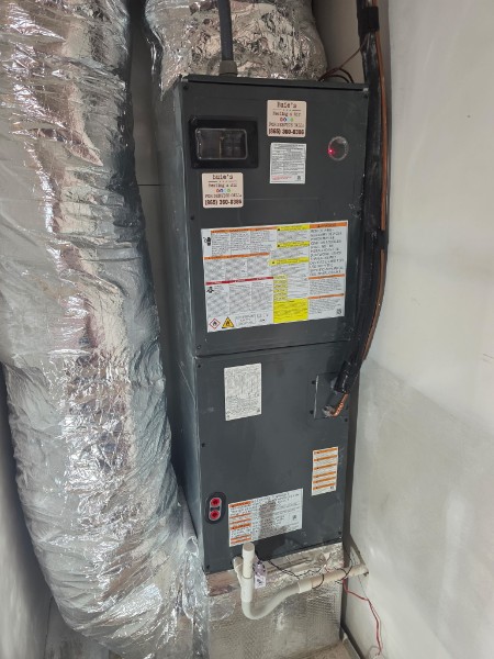 A vertical HVAC unit with metal ducts and various instruction and warning labels, installed against a wall with visible wiring and piping.