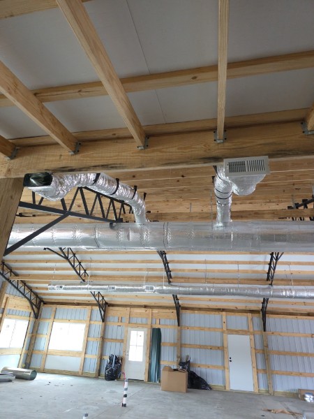 Exposed HVAC ductwork runs along the ceiling of a partially constructed building with wooden beams, metal supports, and unfinished walls.